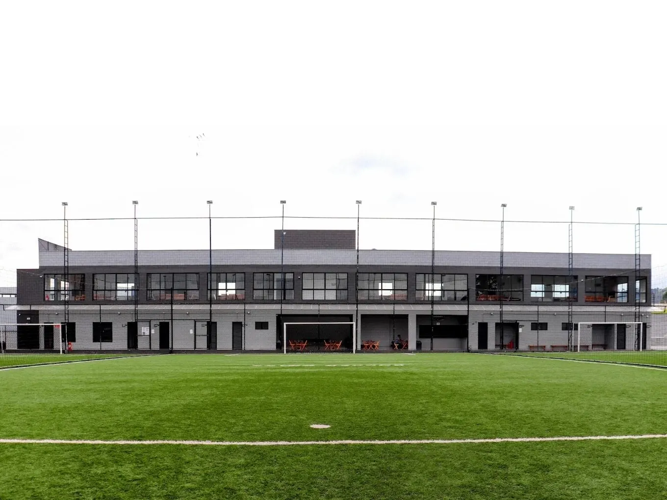 Campo da arena visto da lateral, com o prédio de apoio ao fundo